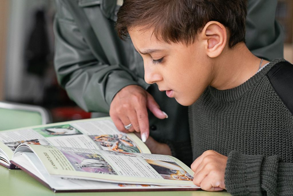 Crafting Captivating Headlines: Your awesome post title goes here Boy concentrating on reading as adult points out text in a book.