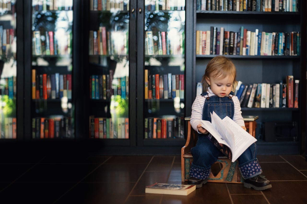 A cute toddler enjoying a book in a cozy library with a book-filled background.